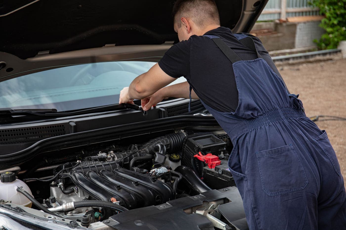 A mechanic leaning over an open engine bay, inspecting a car